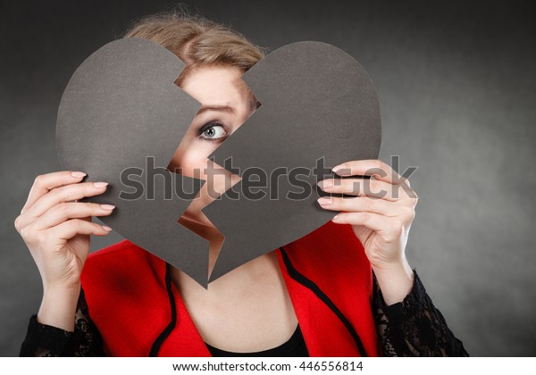 Depression and sadness concept. Young
person with broken heart full of negative sad emotions. Woman
covering his face by two parts of black love
symbol.