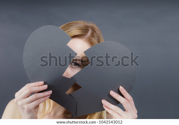 Depression, sadness,\
relationship problem concept. Young female with broken heart full\
of negative sad emotions. Woman covering her face by two parts of\
black love symbol.