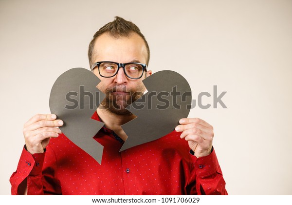 Depression, sadness, relationship
problem concept. Man with broken heart full of negative sad
emotions. Adult male holding two black halves of love symbol, on
grey