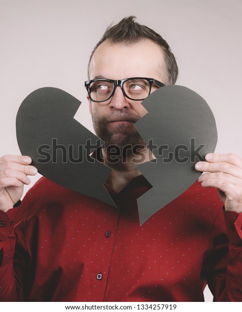 Depression, sadness, relationship
problem concept. Man with broken heart full of negative sad
emotions. Adult male holding two black halves of love symbol, on
grey