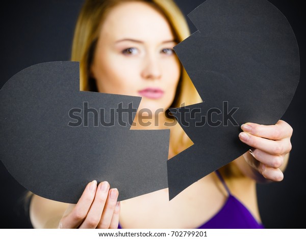 Depression, sadness,
relationship problem concept. Young female with broken heart full
of negative sad emotions. Woman covering her face by two parts of
black love symbol.