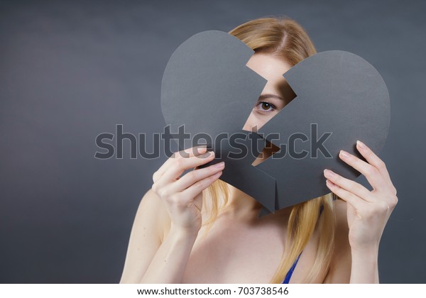 Depression, sadness,
relationship problem concept. Young female with broken heart full
of negative sad emotions. Woman covering her face by two parts of
black love symbol.