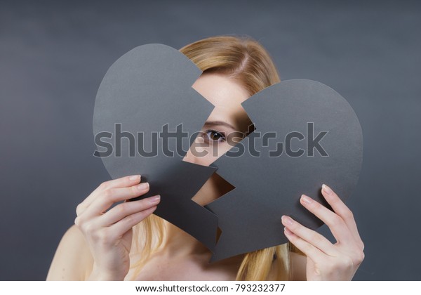 Depression, sadness,\
relationship problem concept. Young female with broken heart full\
of negative sad emotions. Woman covering her face by two parts of\
black love symbol.