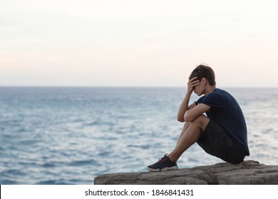 Depression and sadness. Troubled young man sitting alone on a cliff near the ocean. - Powered by Shutterstock