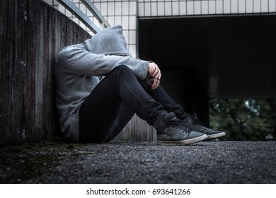 Depression, social isolation, loneliness, mental health and discrimination concept. Sad, lonely, depressed and unhappy man. Hooded person sitting in dark alley.