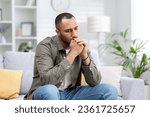 Depression in a young Latin American man sitting thoughtfully and upset at home on the couch.