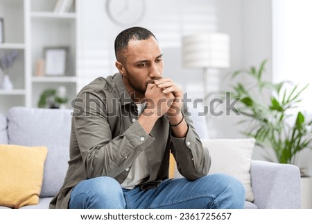 Depression in a young Latin American man sitting thoughtfully and upset at home on the couch.