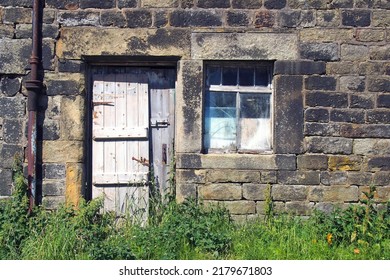 derelict abandoned old stone house with broken window and shabby wooden door overgrown with weeds