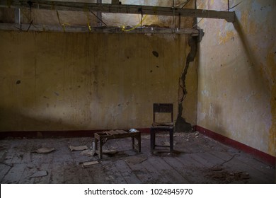 A Derelict Abandoned Room, With Water-stained Peeling Walls, And A Broken Old Wood Table And Chair On Dirty Wood Floorboards.