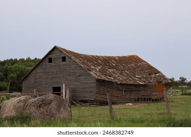 derelict barn with sagging roof behind fence and hay bales - Powered by Shutterstock