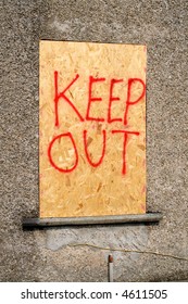 A derelict building with a boarded up window and keep out sign.