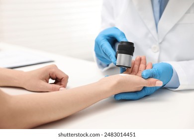 Dermatologist with dermatoscope examining patient at white table in clinic, closeup - Powered by Shutterstock