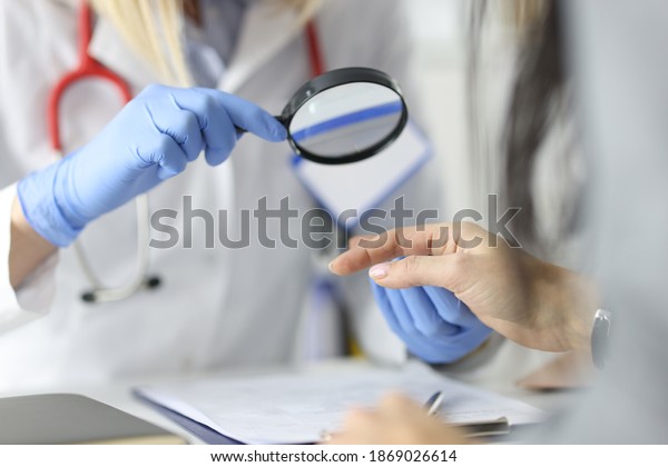 Dermatologist doctor looking at patients skin on\
hands using magnifying glass in clinic closeup. Diagnosis of fungal\
skin diseases\
concept