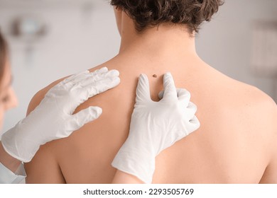Dermatologist examining mole on young man's back in clinic, closeup - Powered by Shutterstock