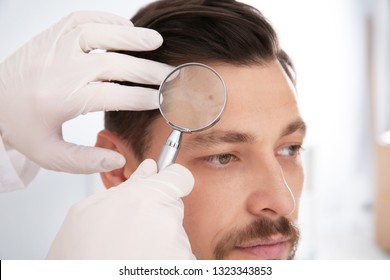 Dermatologist examining patient's birthmark with magnifying glass in clinic - Powered by Shutterstock