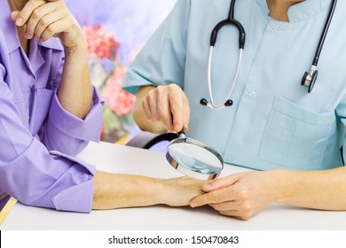 Dermatologist looking at woman's hand through a magnifying glass - Powered by Shutterstock