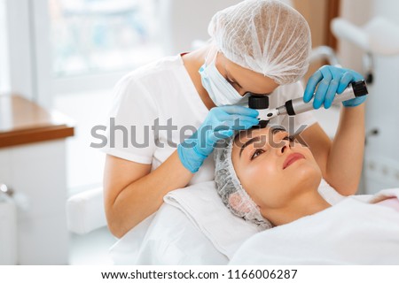 Dermatology clinic. Skilled female dermatologist using a professional dermatoscope while doing the skin examination