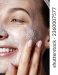 Dermatology. Exfoliating. Skin care facial scrub. Beauty portrait of young happy woman is applying white peeling cosmetic product to whole her face. Daily skincare routine. Dermatology. Exfoliating