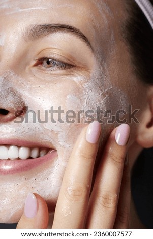 Dermatology. Exfoliating. Skin care facial scrub. Beauty portrait of young happy woman is applying white peeling cosmetic product to whole her face. Daily skincare routine. Dermatology. Exfoliating