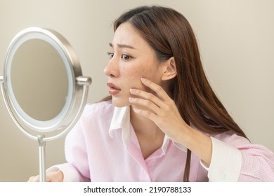 Dermatology, expression face worry asian young woman looking mirror hand touch facial at dark spot of melasma, freckles from pigment melanin, allergy sun. Beauty care, skin problem treatment, skincare