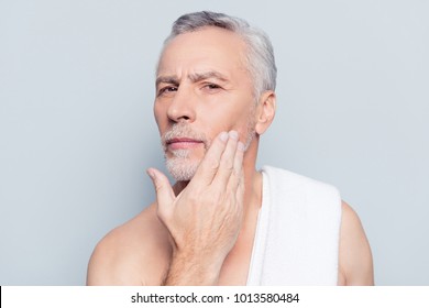 Dermatology pampering procedure rejuvenation wrinkles concept. Close up portrait of concentrated suspicious attentive man analyzing the skin condition touching with hand isolated on gray background