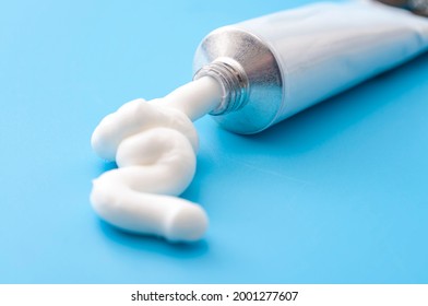 Dermatology, pharmaceutical medicine or healing topical application ointment concept with metal tube pushing white cream isolated on blue background