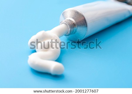 Dermatology, pharmaceutical medicine or healing topical application ointment concept with metal tube pushing white cream isolated on blue background