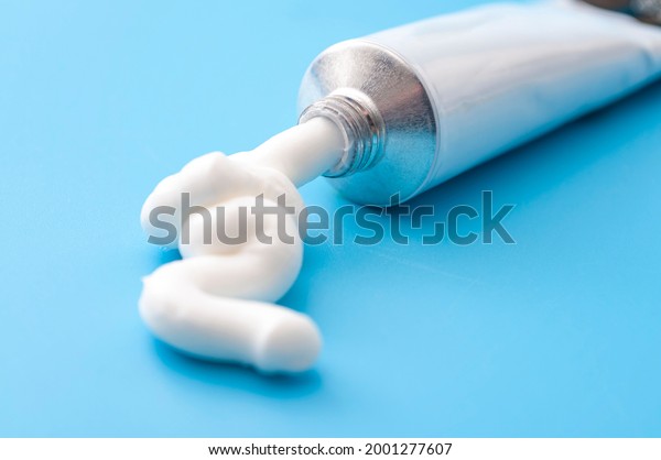 Dermatology, pharmaceutical medicine or\
healing topical application ointment concept with metal tube\
pushing white cream isolated on blue\
background