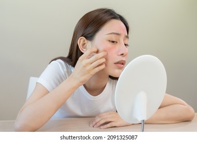 Dermatology, puberty asian young woman, girl looking into mirror, allergy presenting an allergic reaction from cosmetic, red spot or  rash on face. Beauty care from skin problem by medical treatment. - Shutterstock ID 2091325087