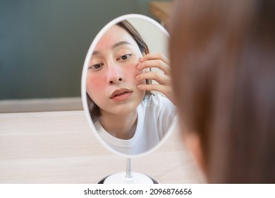 Dermatology, puberty asian young woman, girl looking into mirror, allergy presenting an allergic reaction from cosmetic, red spot or  rash on face. Beauty care from skin problem by medical treatment. - Shutterstock ID 2096876656
