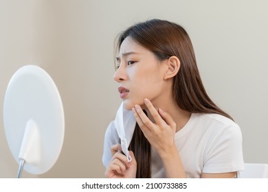 Dermatology, puberty asian young woman, girl looking into mirror, allergy when wear mask and cosmetic, show squeezing pimple spot for removing from face.Beauty care from skin problem by acne treatment