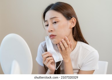 Dermatology, puberty asian young woman, girl looking into mirror, allergy when wear mask and cosmetic, show squeezing pimple spot for removing from face.Beauty care from skin problem by acne treatment - Shutterstock ID 2107320329