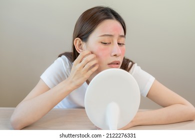 Dermatology, puberty asian young woman, girl looking into mirror, allergy presenting an allergic reaction from cosmetic, red spot or  rash on face. Beauty care from skin problem by medical treatment. - Shutterstock ID 2122276331
