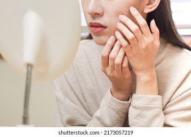 Dermatology, puberty asian young woman, girl looking into mirror, allergy presenting an allergic reaction from cosmetic, red spot or  rash on face. Beauty care from skin problem by medical treatment. - Shutterstock ID 2173057219