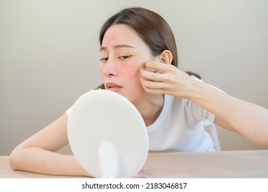 Dermatology, puberty asian young woman, girl looking into mirror, allergy presenting an allergic reaction from cosmetic, red spot or  rash on face. Beauty care from skin problem by medical treatment. - Shutterstock ID 2183046817