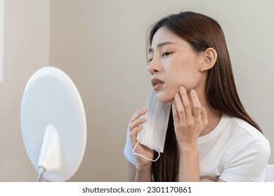 Dermatology, puberty asian young woman, girl looking into mirror, allergy when wear mask and cosmetic, show squeezing pimple spot for removing from face.Beauty care from skin problem by acne treatment - Shutterstock ID 2301170861