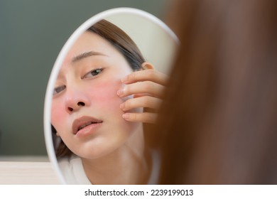 Dermatology, scratch asian young woman looking at mirror, expression worry and itch, itchy allergy or allergic sensitive reaction, red spot or rash on her face. Beauty care from skin problem treatment - Shutterstock ID 2239199013
