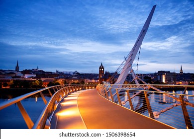 Derry, Ireland. Illuminated Peace bridge in Derry Londonderry, City of Culture, in Northern Ireland with city center at the background. Night cloudy sky with reflection in the river at the dusk
