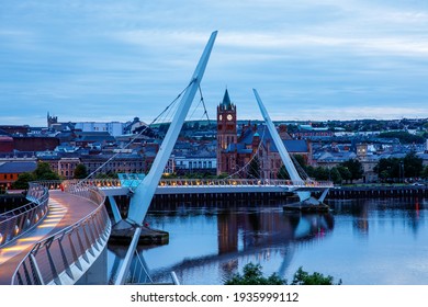 Derry, Ireland. Illuminated Peace bridge in Derry Londonderry, City of Culture, in Northern Ireland with city center at the background. Night cloudy sky with reflection in the river at the dusk