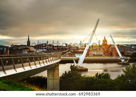 Derry, Ireland. Peace bridge in Derry Londonderry in Northern Ireland with city center at the background. Sunny evening with cloudy sky, reflection in the river