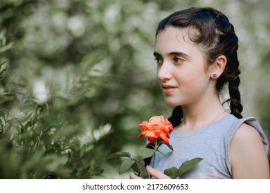 Desatuarted portrait of little armenian girl standing next to the tree in garden and holding the rose