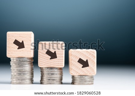 Descending finance graph, decrease coins heap with arrow sign on wood block as graph symbol, business and econnomic recession, credit decrease or less saving money