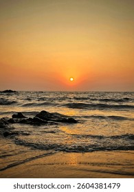 Description: A mesmerizing sunset over a tranquil beach, with golden light reflecting on gentle waves and rocky shores, creating a peaceful and serene scene.
