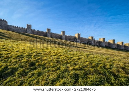 DescriptionThe work was started in 1090 but most of the defensive wall appears to have been rebuilt in the 12th century. The enclosed area is an irregular rectangle of 31 hectares with a perimeter of some 2,516 meters, including 88 semicircular towers. The walls have an average width of 3 metres and an average height of 12 metres. The nine gates were completed over several different periods. The Puerta de San Vicente (Gate of St Vincent) and the Puerta del Alcazar (Gate of the Fortress) are flanked by twin towers, 20 metres high, linked by a semicircular arch. The apse of the cathedral also forms one of the towers.It is possible to walk upon the walls for roughly half the circumference. Whilst some of the walls will never be navigable in this way because of their integration into other structures, there is a large stretch of the walls that has yet to be made safe for pedestrians.The site was registered as a National Monument in 1884.I n 1985, the old city of Ávila and its extramural churches were declared a World Heritage site by UNESCO.Source: WikipediaÁvila, Spain. Medieval fortification of Ávila city with stone towers standing on green grassy slope
