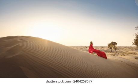 Desert adventure. Young arabian Woman in red silk dress in sands dunes of UAE desert at sunset, fantastic view. The Dubai Desert Conservation Reserve, United Arab Emirates. - Powered by Shutterstock