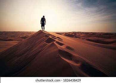 Desert adventure. Young man walking on sand dune against sunset. Abu Dhabi, United Arab Emirates - Powered by Shutterstock