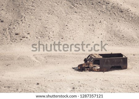 In the desert is a burnt military vehicle.