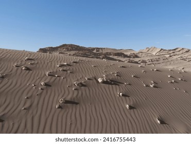 Desert dunes with tiny rocks under the bright blue sky and the moon