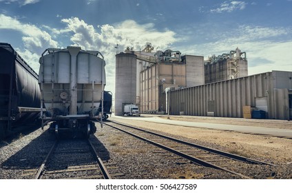 Desert landscape.  Arizona heat beats down on industrial building and rail road track with cargo containers, silo and large facility in distance.