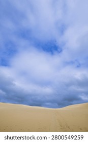 Desert landscape featuring rolling sand dunes under a dramatic cloudy sky